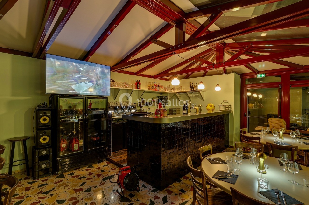 Intérieur d'un restaurant avec un bar, des tables dressées, un écran mural et une ambiance chaleureuse.