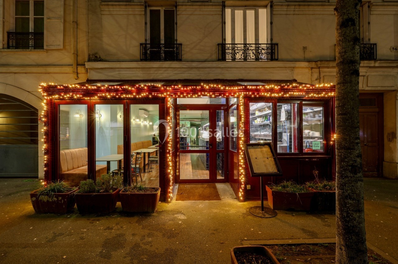 Façade d'un restaurant éclairée par des guirlandes lumineuses, avec des tables visibles à l'intérieur.