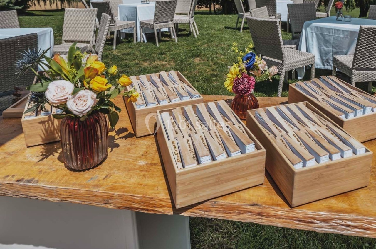 Couverts en bois disposés dans des boîtes sur une table en extérieur, avec des bouquets de fleurs colorées.