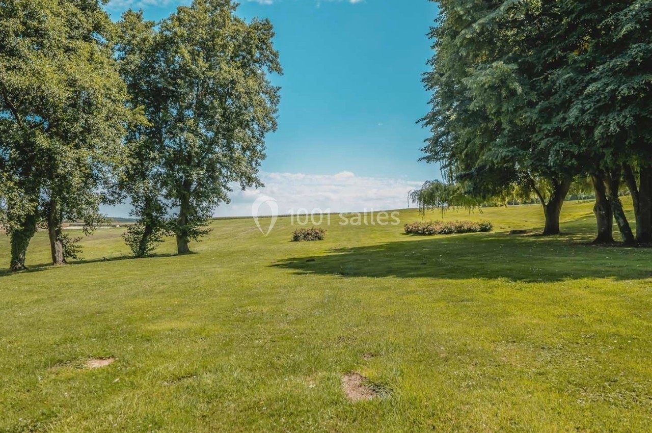 Pelouse verdoyante entourée d'arbres sous un ciel bleu dégagé.