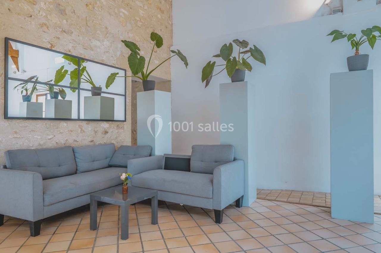 Salon avec deux canapés gris, une table basse, des plantes en pot et un mur en pierre apparente.