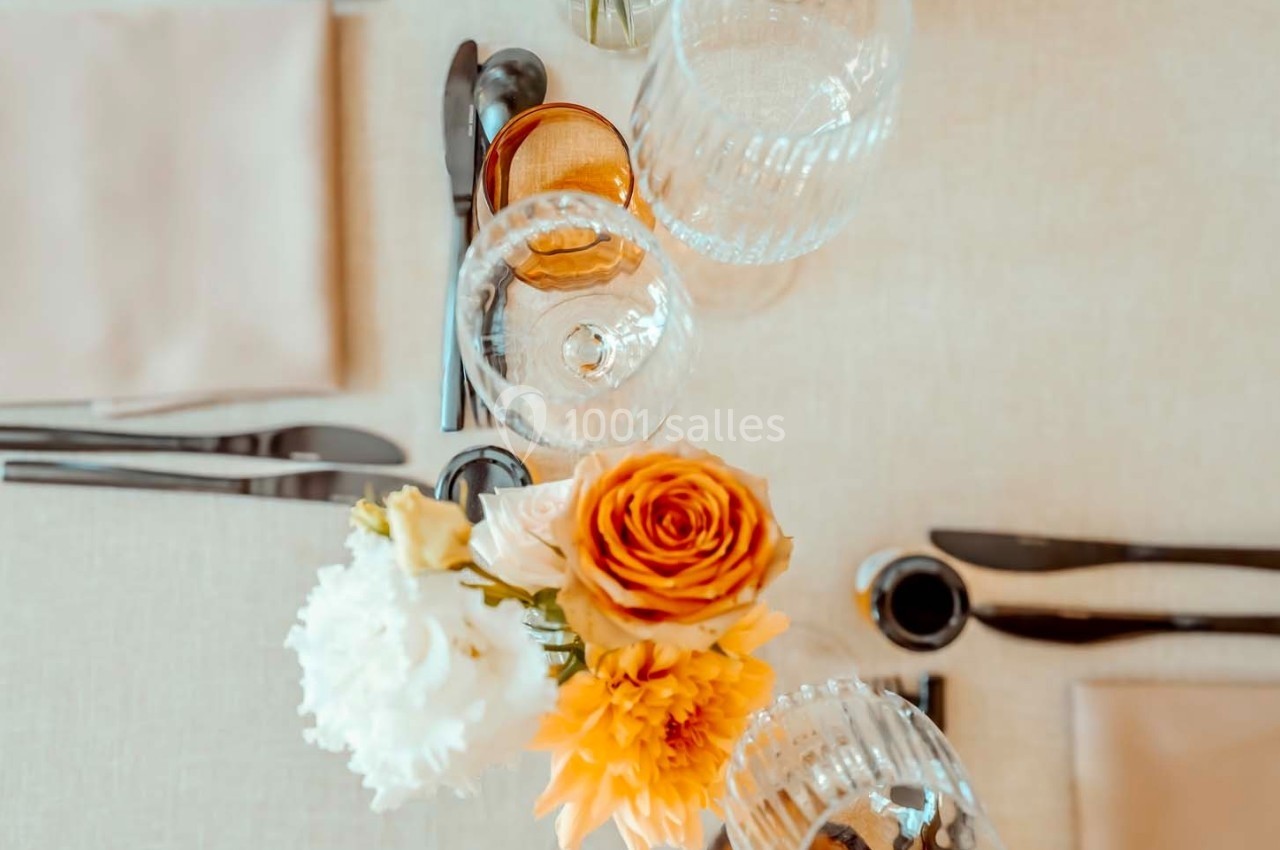 Vue d'une table élégamment dressée avec des verres, des couverts et un bouquet de fleurs colorées au centre.