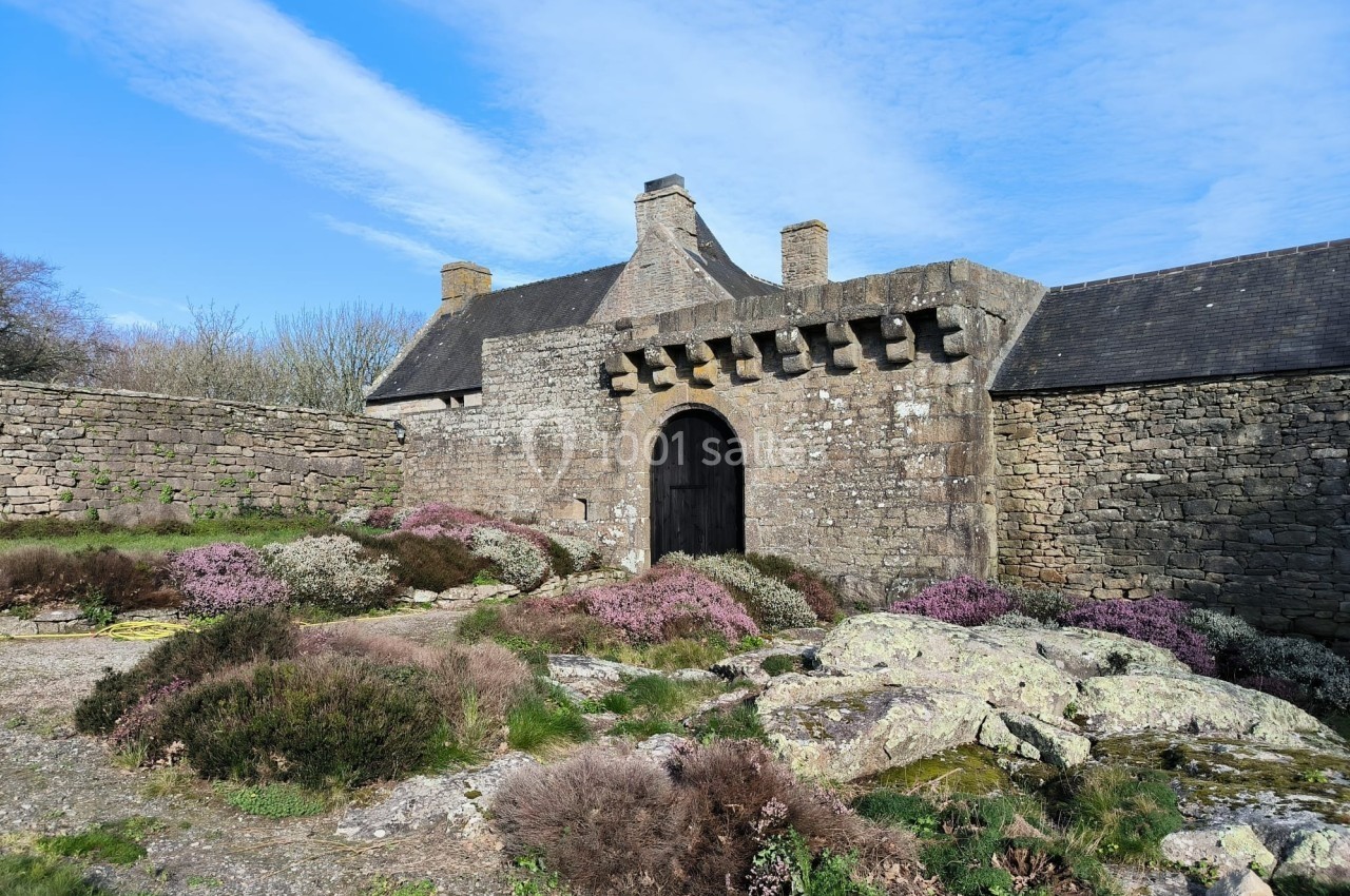 Entrée voûtée d'un bâtiment en pierre entouré de végétation et de rochers sous un ciel bleu.