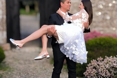 Vue aérienne d'un manoir en pierre entouré de champs et de végétation, avec un village et la mer à l'horizon.