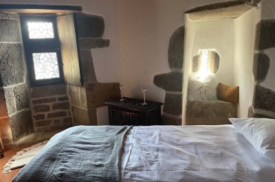 Vue aérienne d'un manoir en pierre entouré de champs et de végétation, avec un village et la mer à l'horizon.