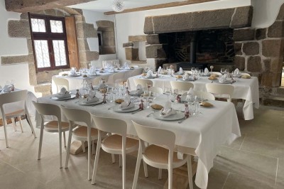 Vue aérienne d'un manoir en pierre entouré de champs et de végétation, avec un village et la mer à l'horizon.