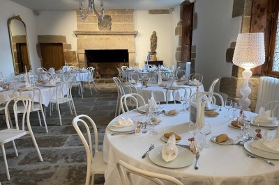 Vue aérienne d'un manoir en pierre entouré de champs et de végétation, avec un village et la mer à l'horizon.