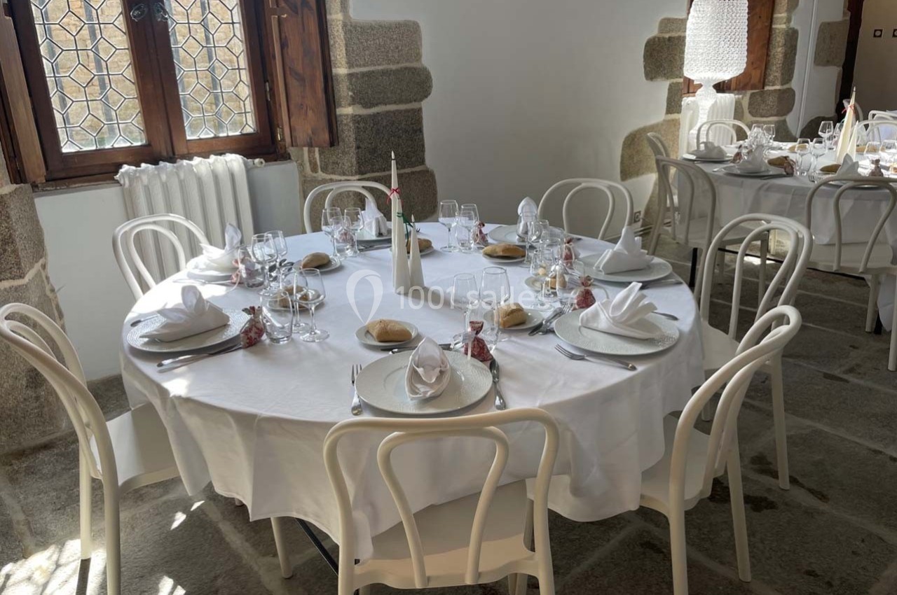 Table ronde dressée pour un repas, avec nappes blanches, assiettes, verres, serviettes pliées et décorations simples.