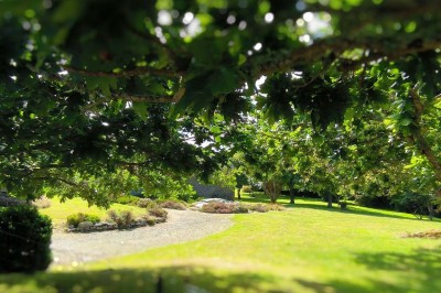 Vue aérienne d'un manoir en pierre entouré de champs et de végétation, avec un village et la mer à l'horizon.