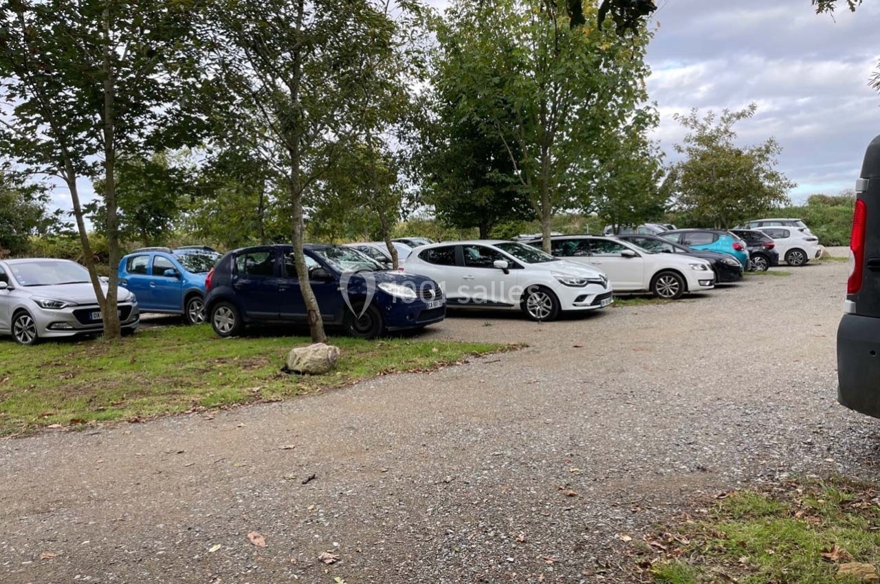 Parking extérieur avec plusieurs voitures stationnées, entouré d'arbres et d'un chemin en gravier.