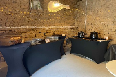 Vue aérienne d'un manoir en pierre entouré de champs et de végétation, avec un village et la mer à l'horizon.