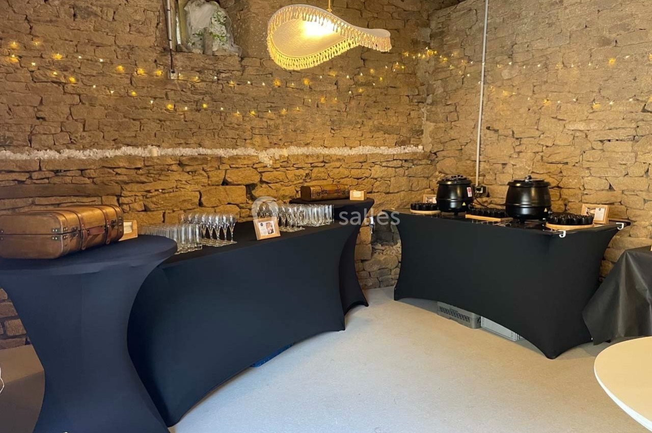 Buffet avec nappes noires, soupières, verres et décorations lumineuses dans une salle en pierre.