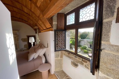 Vue aérienne d'un manoir en pierre entouré de champs et de végétation, avec un village et la mer à l'horizon.