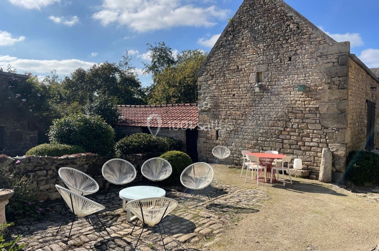 Cour en pierre avec mobilier de jardin moderne, entourée de bâtiments en pierre et végétation sous un ciel dégagé.
