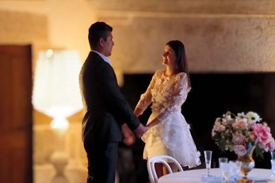 Vue aérienne d'un manoir en pierre entouré de champs et de végétation, avec un village et la mer à l'horizon.