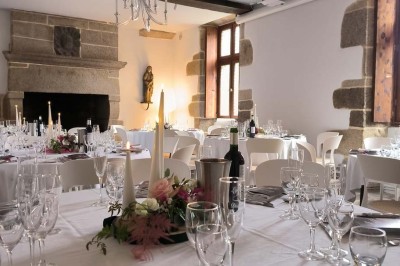 Vue aérienne d'un manoir en pierre entouré de champs et de végétation, avec un village et la mer à l'horizon.
