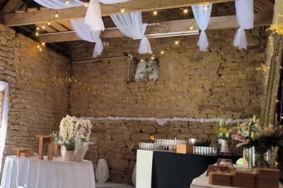 Vue aérienne d'un manoir en pierre entouré de champs et de végétation, avec un village et la mer à l'horizon.