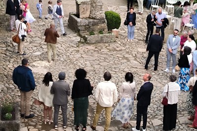 Vue aérienne d'un manoir en pierre entouré de champs et de végétation, avec un village et la mer à l'horizon.