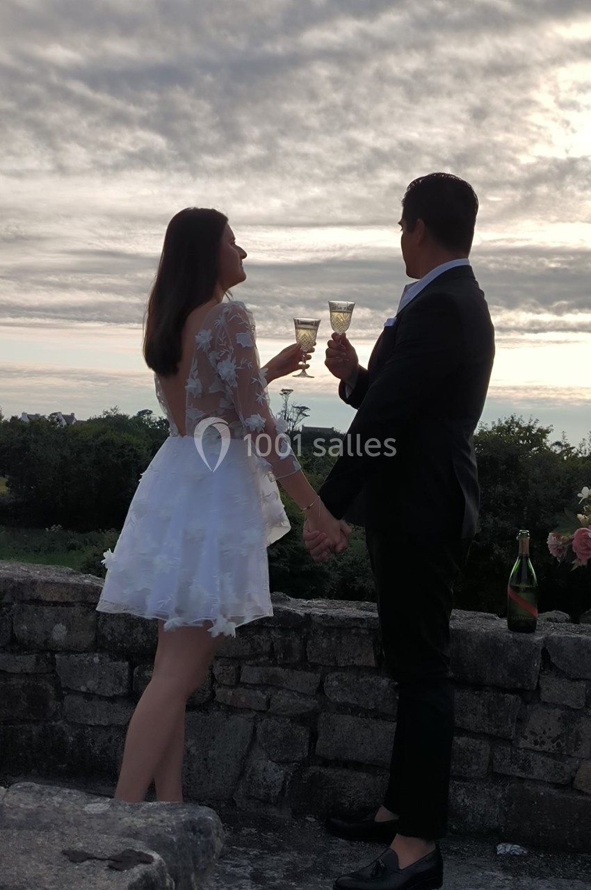 Un couple élégant trinque au champagne devant un paysage naturel au coucher du soleil.