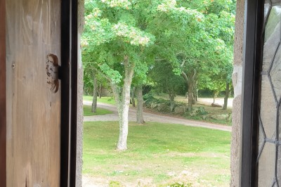Vue aérienne d'un manoir en pierre entouré de champs et de végétation, avec un village et la mer à l'horizon.