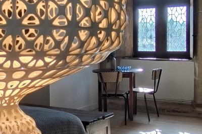 Vue aérienne d'un manoir en pierre entouré de champs et de végétation, avec un village et la mer à l'horizon.