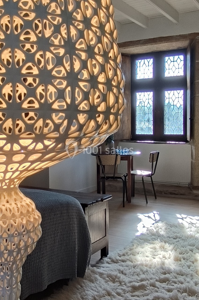 Lampe ajourée illuminée dans une chambre avec tapis en laine, lit, table en bois et fenêtre à vitraux.