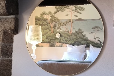 Vue aérienne d'un manoir en pierre entouré de champs et de végétation, avec un village et la mer à l'horizon.