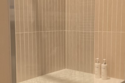 Vue aérienne d'un manoir en pierre entouré de champs et de végétation, avec un village et la mer à l'horizon.