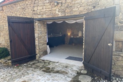 Vue aérienne d'un manoir en pierre entouré de champs et de végétation, avec un village et la mer à l'horizon.