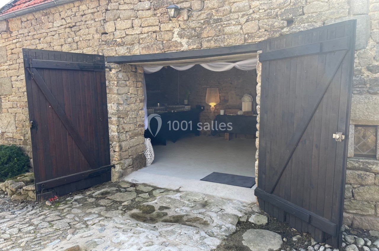 Entrée d'une grange en pierre avec portes en bois ouvertes, dévoilant un intérieur aménagé et éclairé.