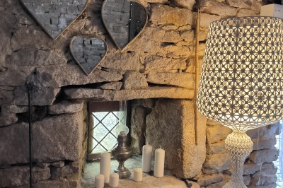 Vue aérienne d'un manoir en pierre entouré de champs et de végétation, avec un village et la mer à l'horizon.