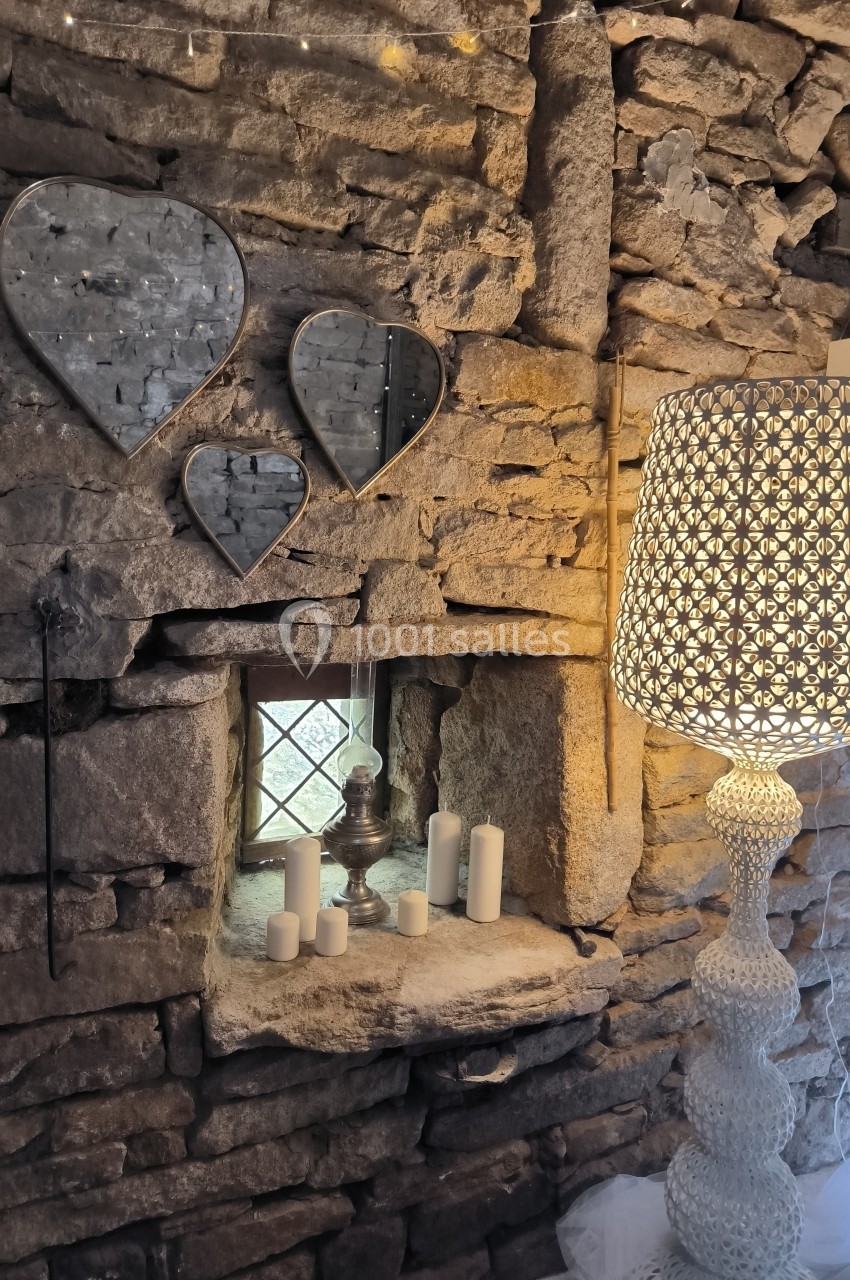 Mur en pierre avec une niche contenant des bougies et un vase, décoré de miroirs en forme de cœur et d'une lampe à motifs.