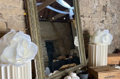 Vue aérienne d'un manoir en pierre entouré de champs et de végétation, avec un village et la mer à l'horizon.