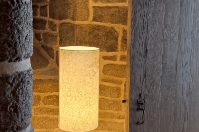 Vue aérienne d'un manoir en pierre entouré de champs et de végétation, avec un village et la mer à l'horizon.