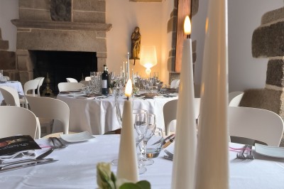 Vue aérienne d'un manoir en pierre entouré de champs et de végétation, avec un village et la mer à l'horizon.