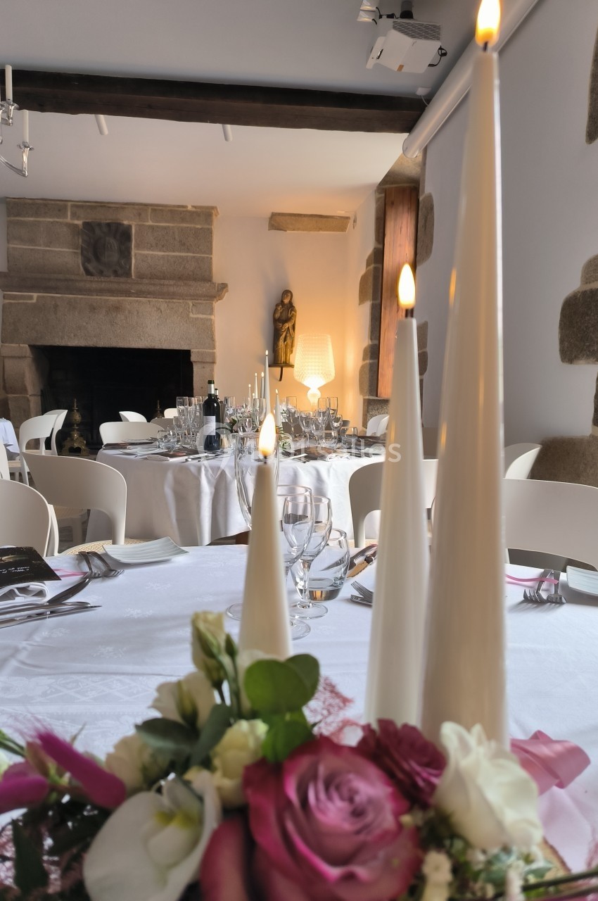 Salle de réception élégante avec tables dressées, chandelles allumées et bouquet de fleurs au premier plan.