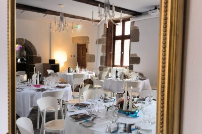 Vue aérienne d'un manoir en pierre entouré de champs et de végétation, avec un village et la mer à l'horizon.