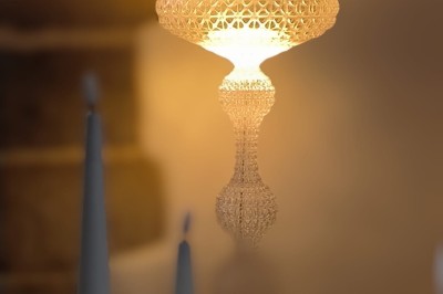 Vue aérienne d'un manoir en pierre entouré de champs et de végétation, avec un village et la mer à l'horizon.