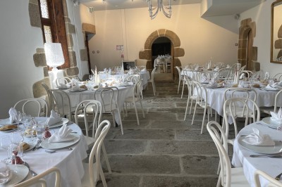 Vue aérienne d'un manoir en pierre entouré de champs et de végétation, avec un village et la mer à l'horizon.
