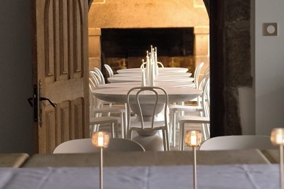 Vue aérienne d'un manoir en pierre entouré de champs et de végétation, avec un village et la mer à l'horizon.