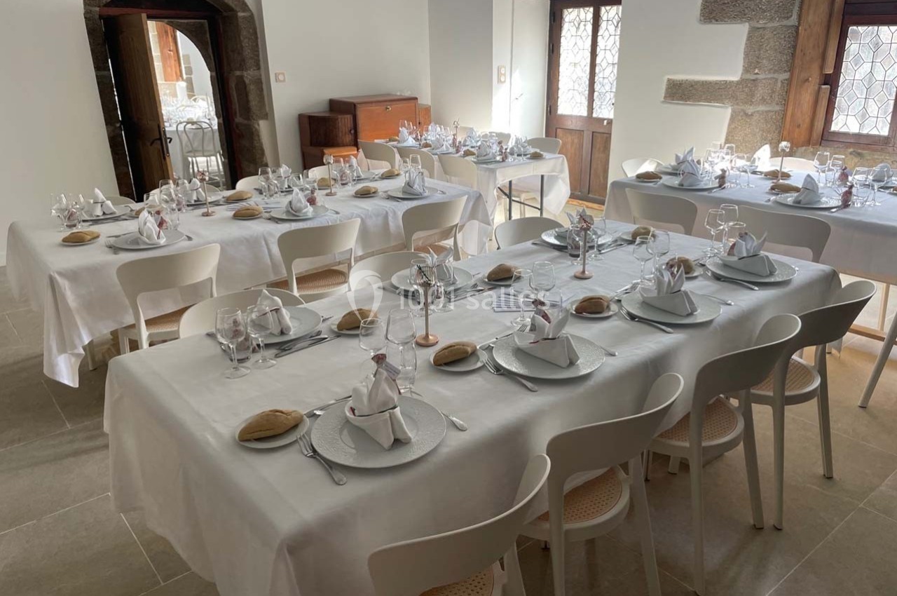 Salle lumineuse avec tables dressées pour un repas, nappes blanches, vaisselle élégante et pain disposé sur chaque couvert.