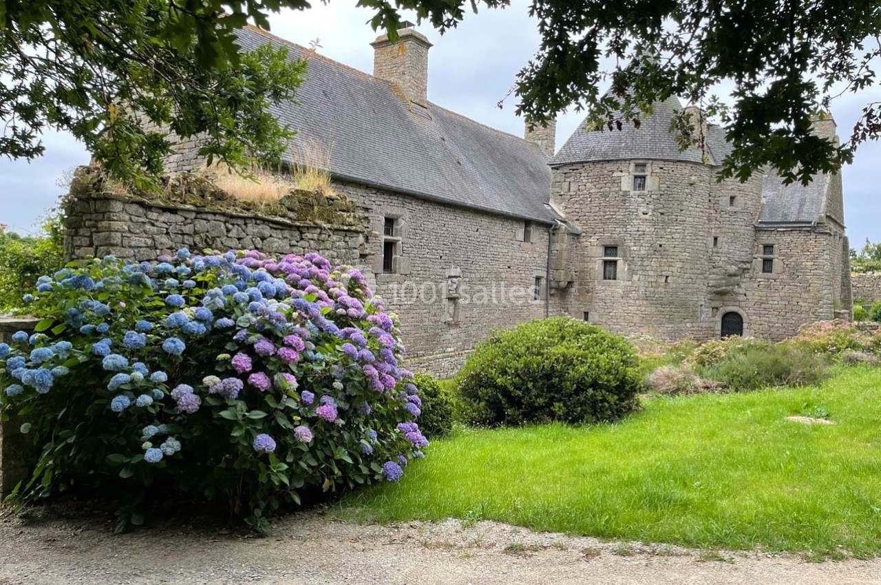 Vieille bâtisse en pierre entourée de verdure, avec des hortensias en fleurs au premier plan.