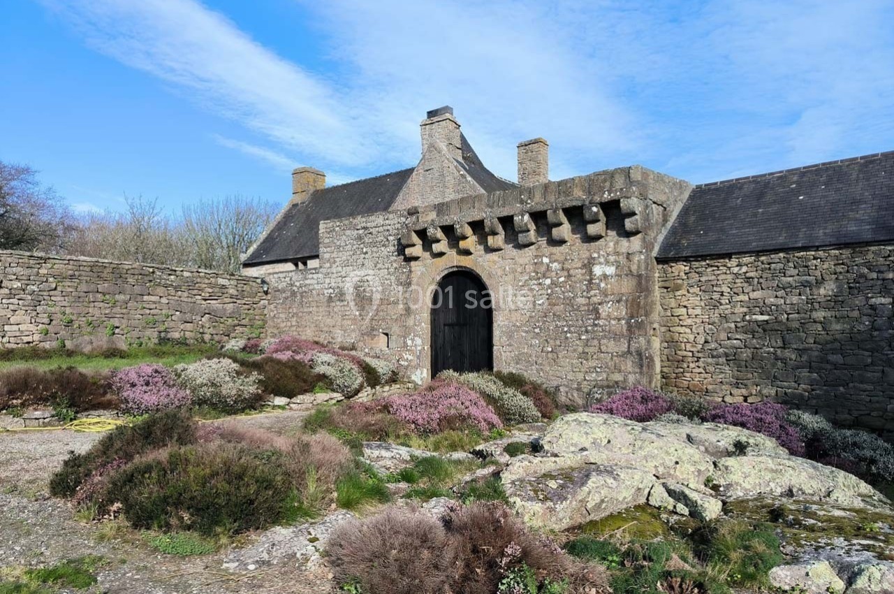 Entrée en pierre d'un bâtiment ancien entourée de végétation et de rochers sous un ciel bleu.