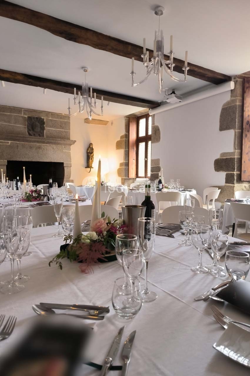 Salle de réception élégante avec tables dressées, chandeliers suspendus et cheminée en pierre.