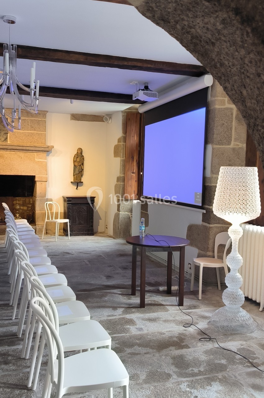 Salle de réunion avec chaises blanches alignées, écran de projection allumé et éléments de décoration en pierre.
