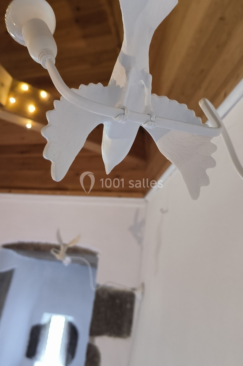 Suspension en forme d'oiseau blanc avec des ailes déployées, accrochée à un plafond en bois dans une pièce lumineuse.