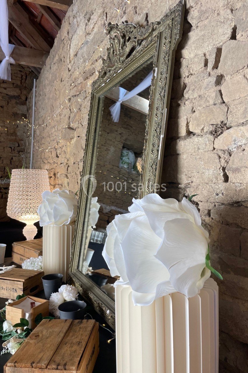 Grand miroir doré posé contre un mur en pierre, entouré de décorations blanches et d'objets en bois.