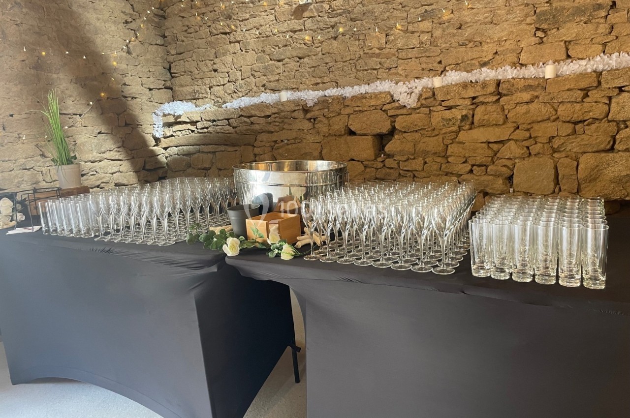 Tables noires dressées avec des rangées de flûtes à champagne et un seau à glace dans une salle en pierre décorée.