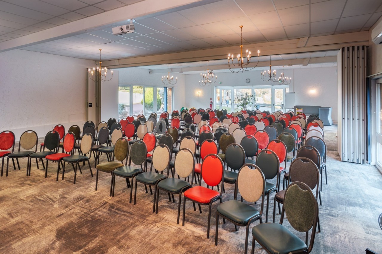Salle de conférence lumineuse avec rangées de chaises colorées disposées face à un espace de présentation.