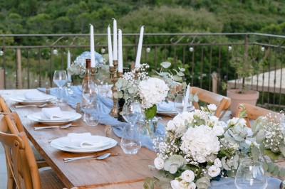 Table dressée avec nappes blanches, vaisselle vintage, chandeliers et décorations florales séchées.